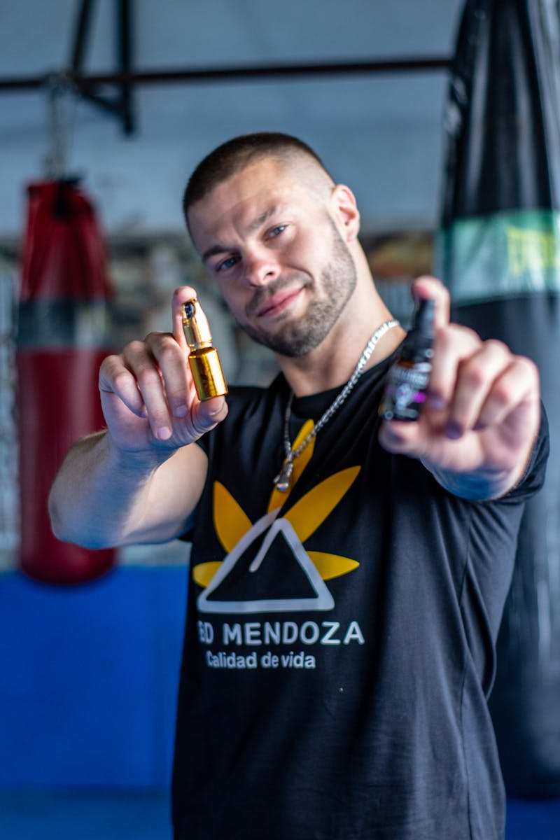 Young man showcases CBD oil bottles in a gym, emphasizing wellness and fitness.