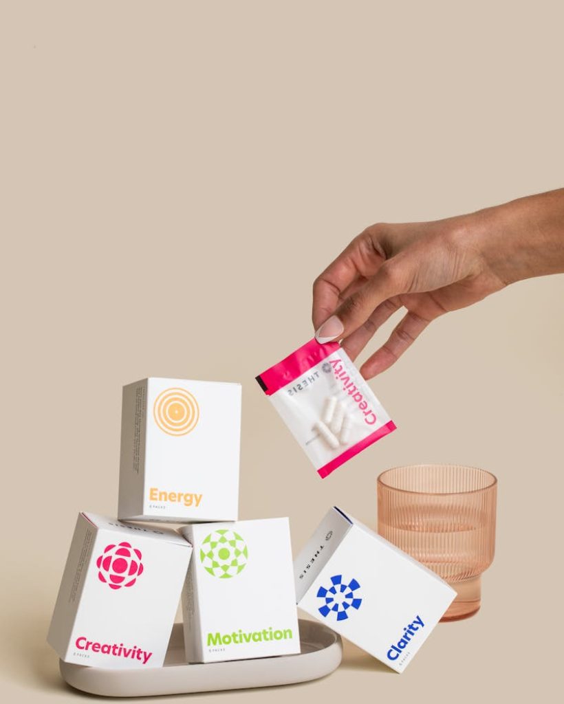 Hand holding a sachet above a stack of supplement boxes with glass, symbolizing vitamins.