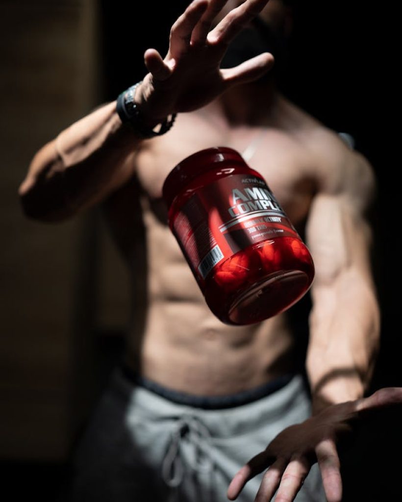 Complementos vitaminicos Barcelona - A shirtless man skillfully tosses a supplement jar in a dramatic indoor setting, showcasing fitness and agility.